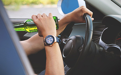obrázek muže s lahví alkoholu za volantem. Ilustrační obrázek pro odkaz do sekce Články